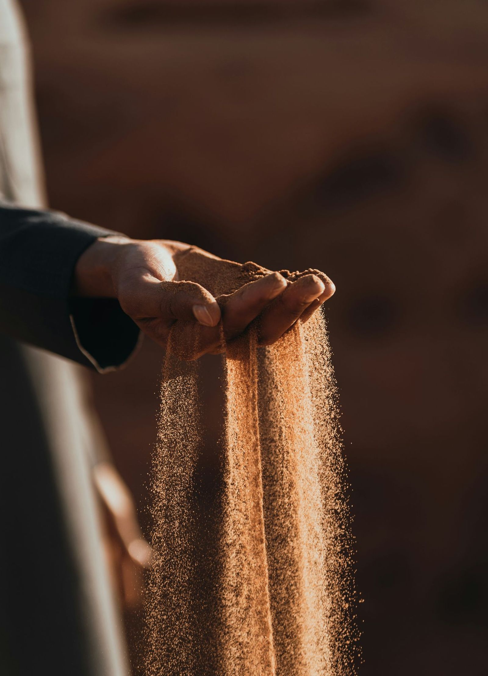 Hands letting sand flow between fingers, warm lighting, textured grains