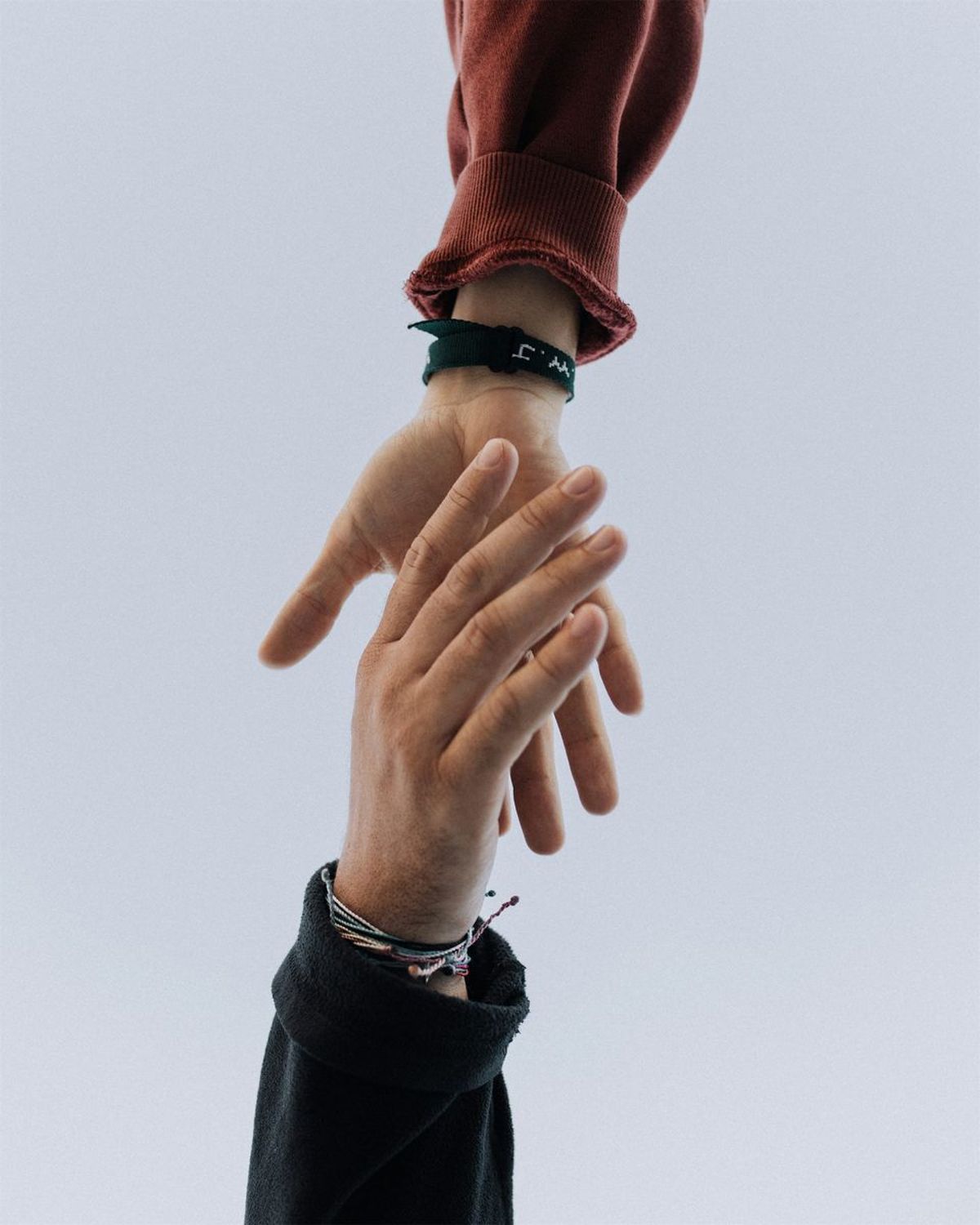 Two hands reaching towards each other, one in red sleeve, one in black sleeve, close-up