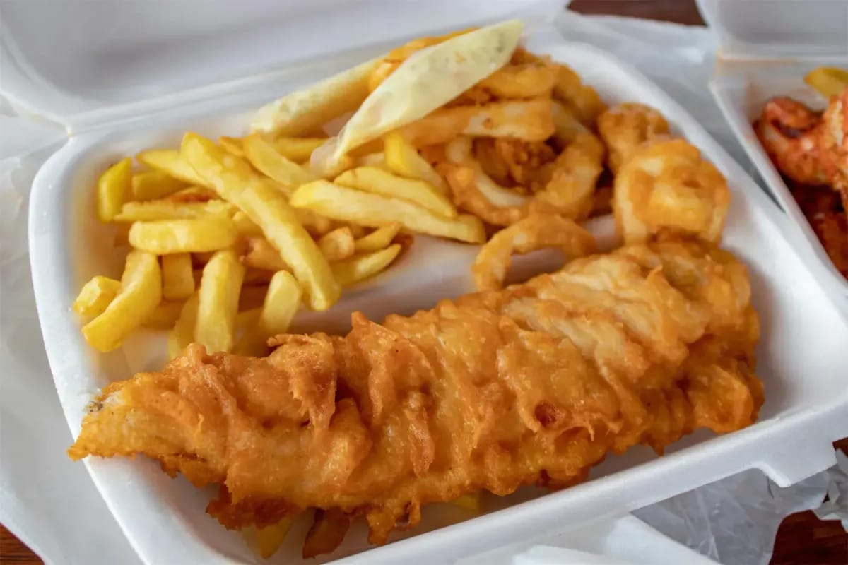 Golden crispy fish and chips in white takeout container with onion rings